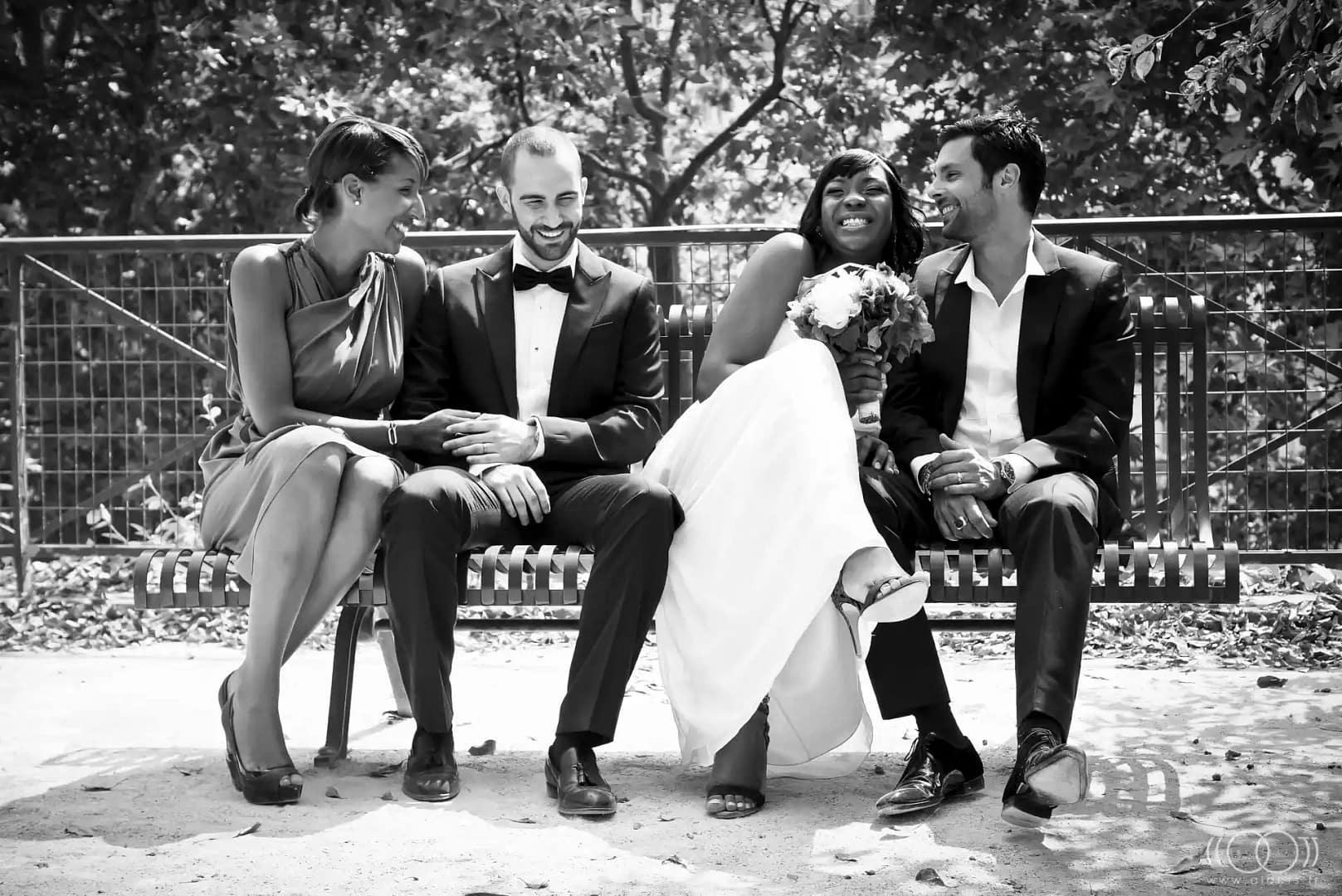 photo en noir et blanc d'un couple mixte assis sur un banc entouré d'un couple d'amis. Ils rigolent ensemble