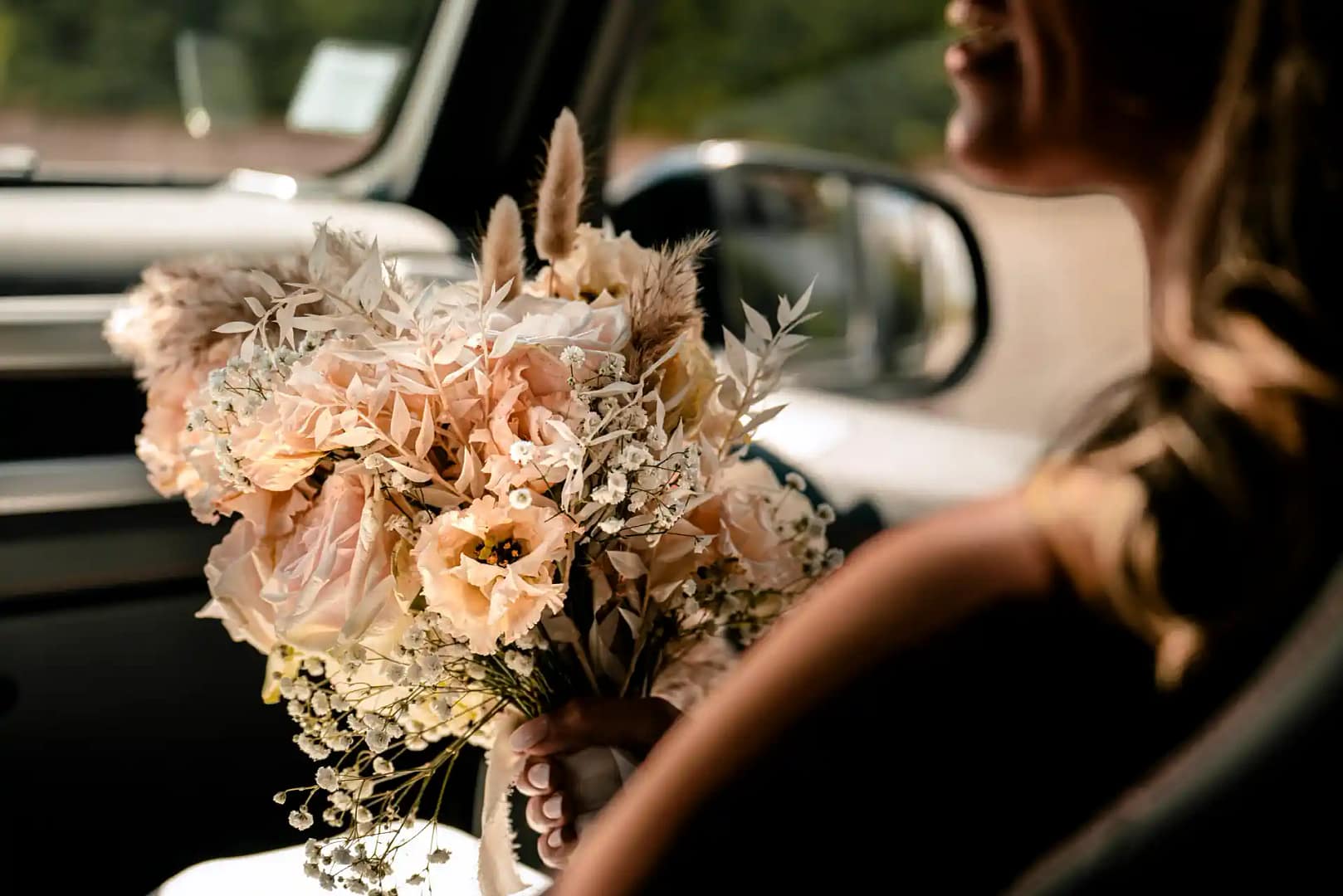 vue intérieure d'une voiture : la mariée porte à la main un bouquet dans des tons chauds