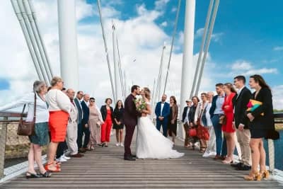couple de mariés s'embrassant sur un pont entouré de leurs familles