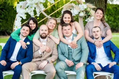 groupe d'amis à un mariage. Les épouses sont debout et enlacent leurs maris qui sont assis devant elles