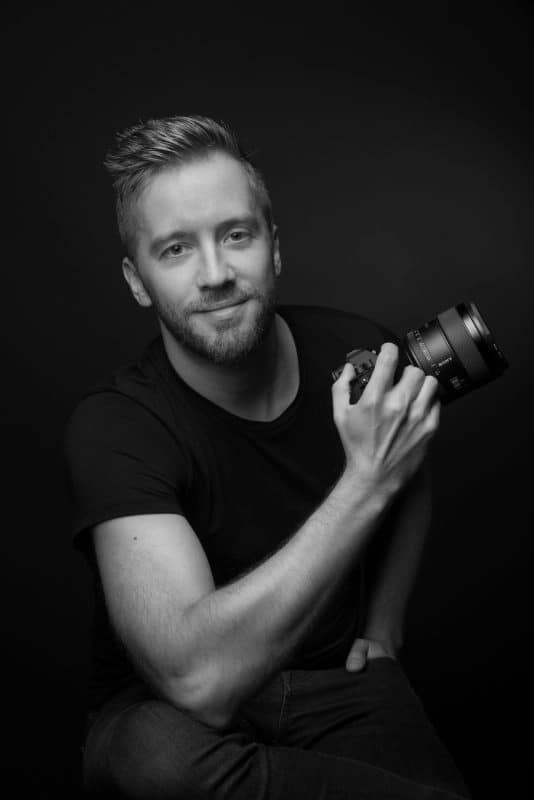 photo en noir et blanc du photographe Arnaud Loots, assis, tenant son appareil photo à la main