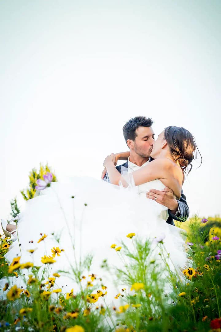couple de mariés qui s'embrasse dans un champ de fleurs